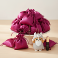 Premier Scoop — 10 magenta satin drawstring pouches piled in a white ceramic dish, with Mofusand cat plush keychain, gold necklace, and luxury perfume or lotion spilling out