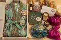 The Deep Dive — open kraft gift box with cream tissue, intricate sage green floral kimono robe, ornate cloisonné teapot set, body oil, silver hoop earrings, rose sachet, vintage book, handmade lotion, amber glass candle, and magenta satin drawstring bags